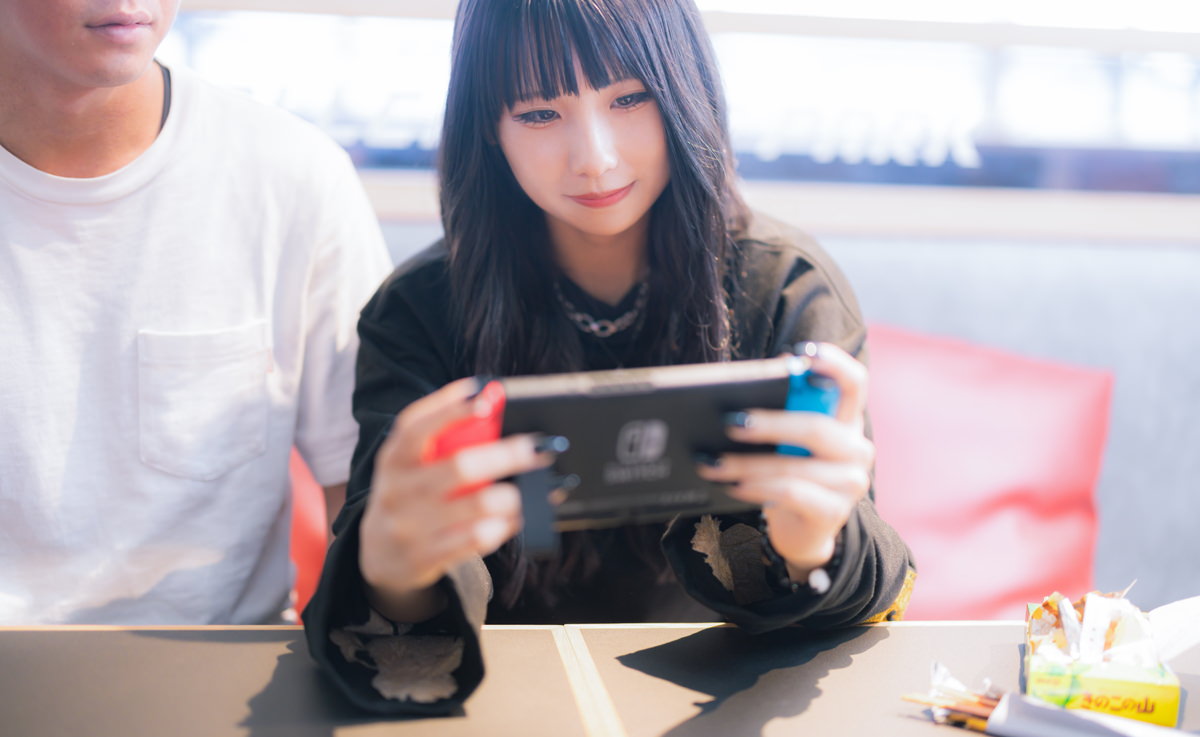 彼氏と一緒に携帯ゲーム機をプレイする女性の無料写真素材