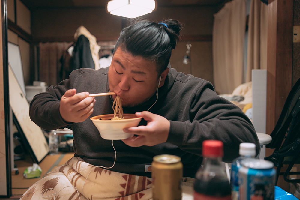 散らかった部屋でラーメンを食べる肥満男子