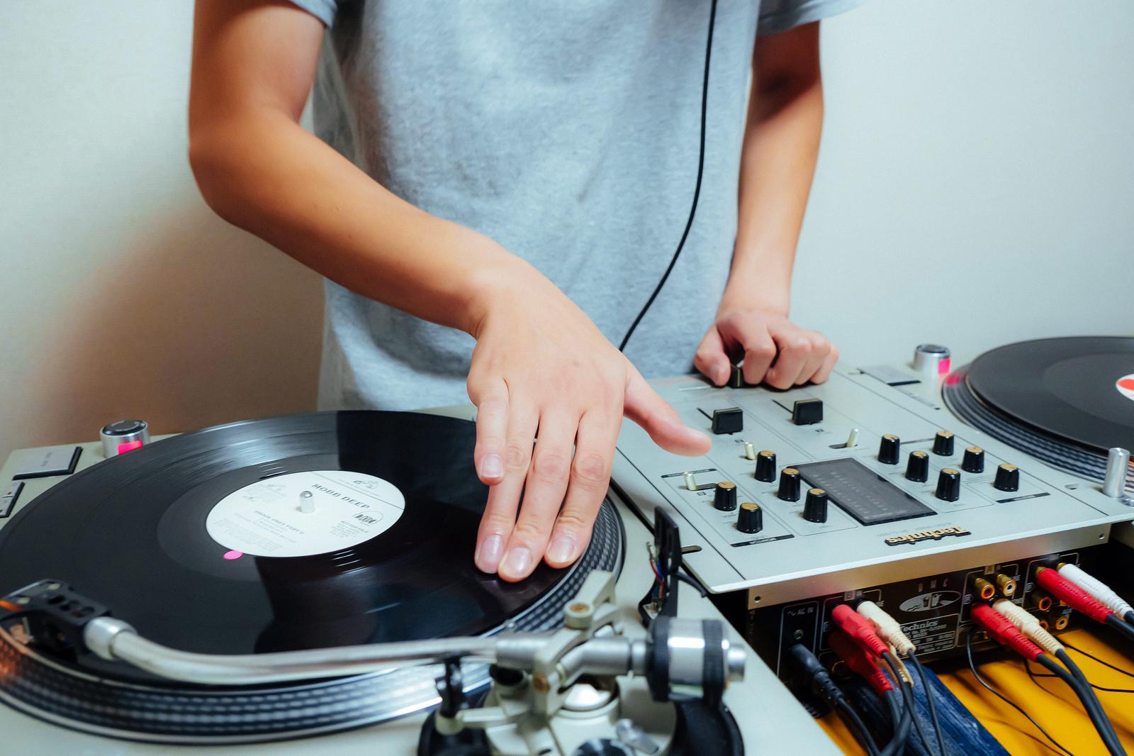 グレーのTシャツを着たDJがレコードを操作しながらミキサーで音楽を調整している