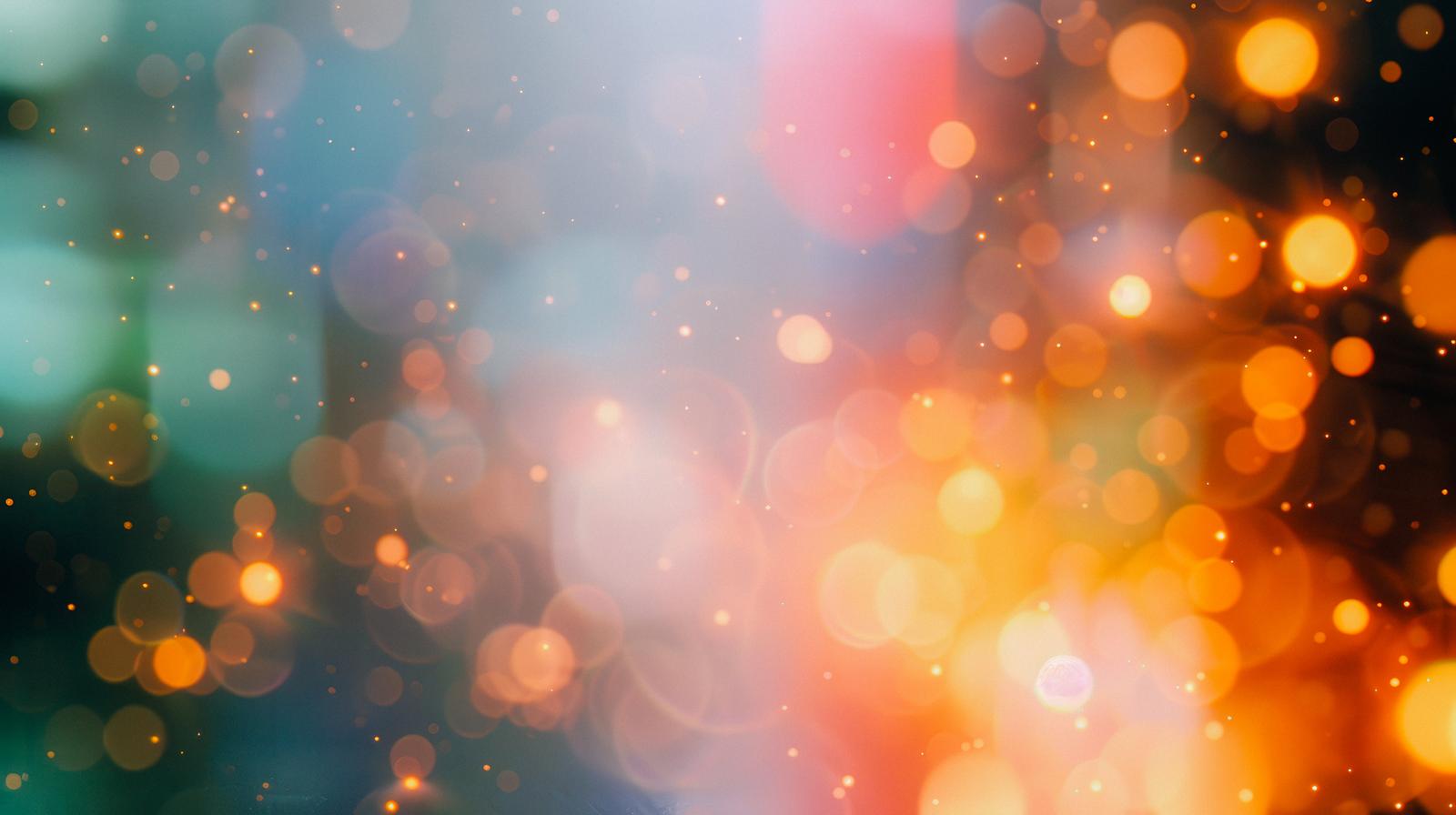 青緑色からオレンジ黄色に変わるグラデーションに、ボケた光の粒が浮かぶ背景