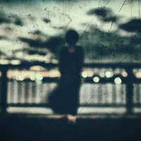 屋上のフェンス越しに立つ黒い人影のシルエットの写真