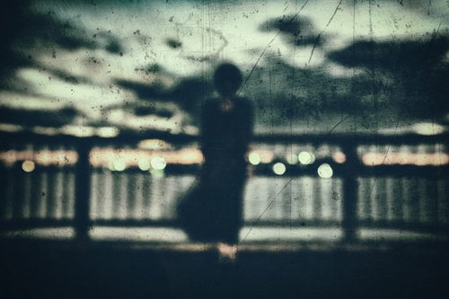 屋上のフェンス越しに立つ黒い人影のシルエット