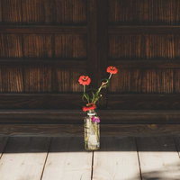 寺前の木製棚に置かれた花瓶に活けたガーベラの写真