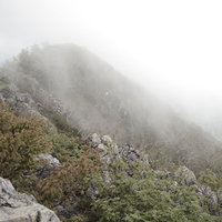 ガスに包まれる高妻山の稜線と岩場を行く登山者の景観の写真