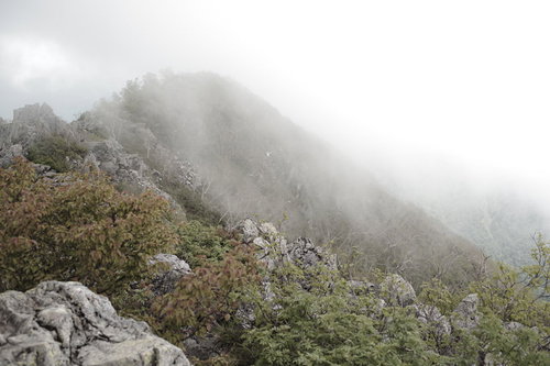 ガスに包まれる高妻山の稜線と岩場を行く登山者の景観