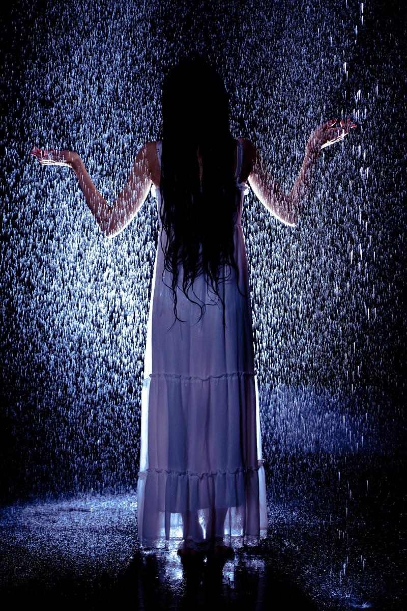 激しい雨に打たれびしょ濡れになった紫のドレス姿の女性の後ろ姿［モデル：緋真煉］