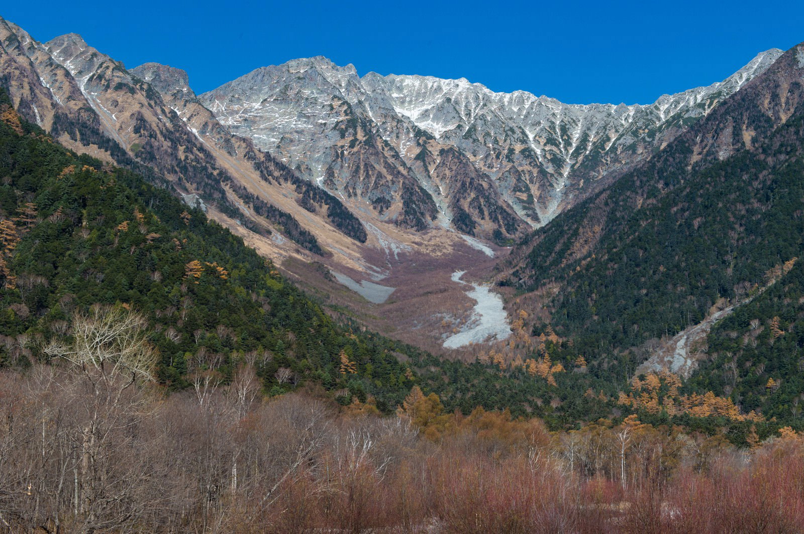 青空の下、雪化粧した穂高連峰と紅葉した渓谷を上高地から撮影した山岳風景