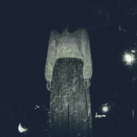 仄暗い闇の奥から立つ白い衣服の女性の怪奇的な人影の写真