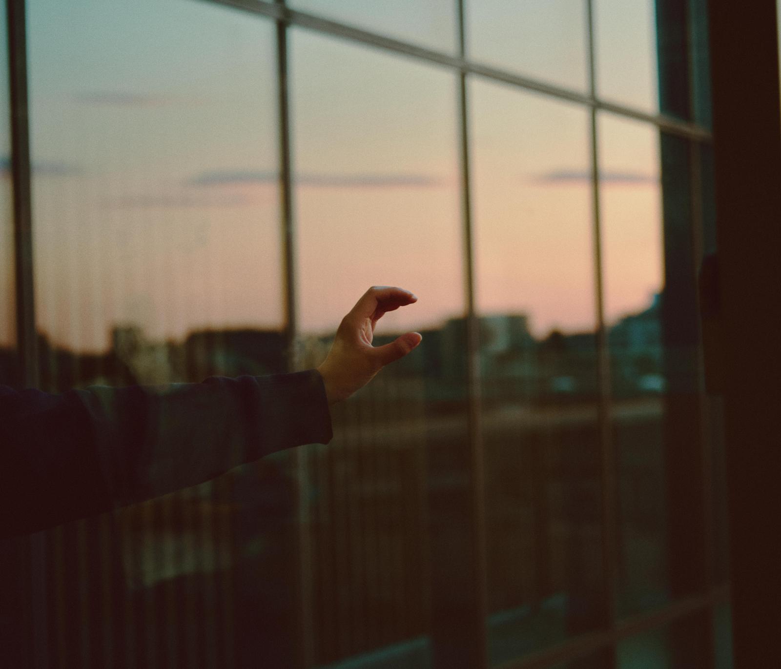 夕暮れの窓の前で左手でCのジェスチャーをする人物