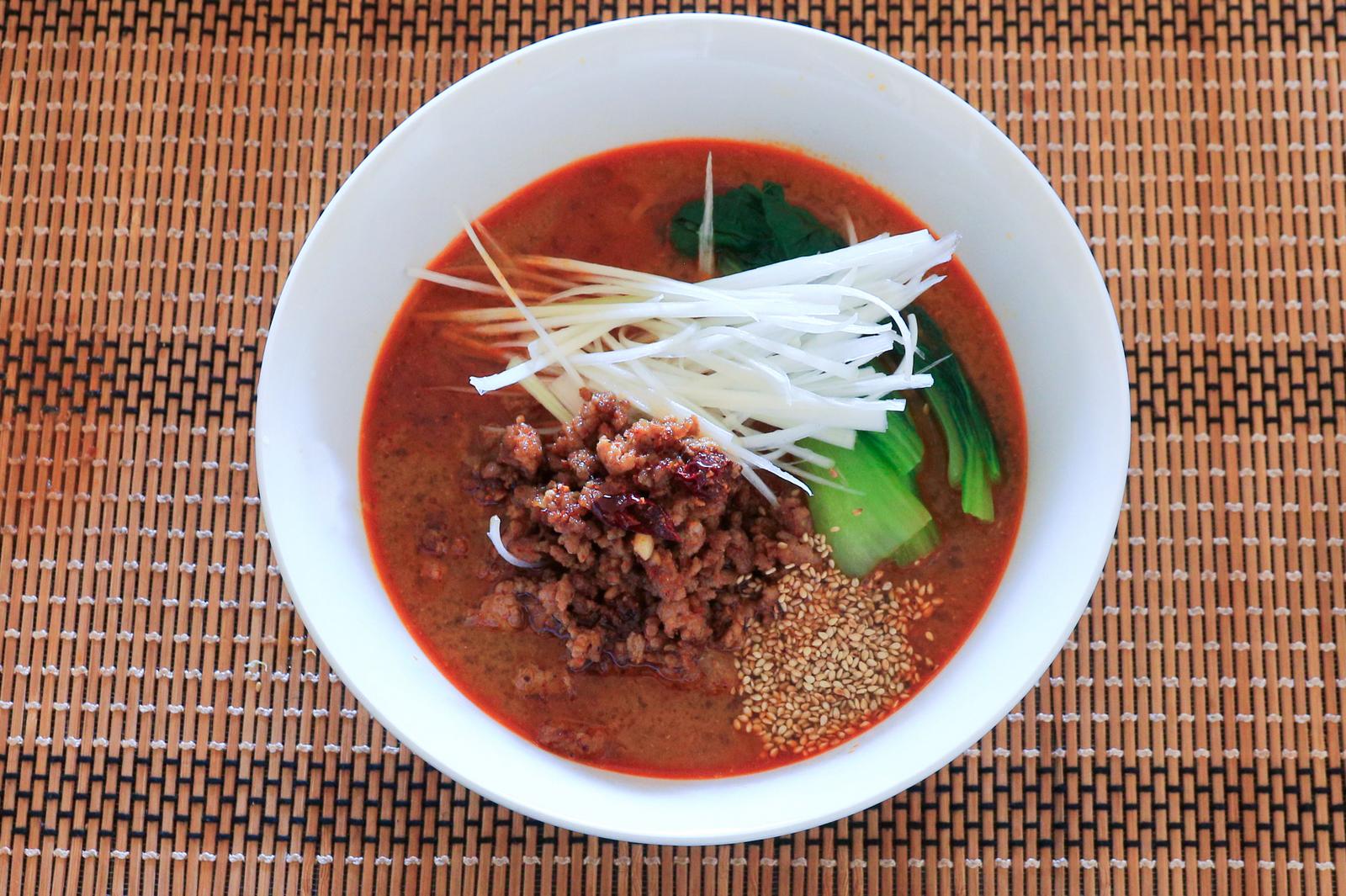 Overhead view of Tantan noodles (Tantanmen) topped with spiced meat sauce (Nikumiso) and shredded Welsh onion (Shiraga negi) placed on a bamboo placemat