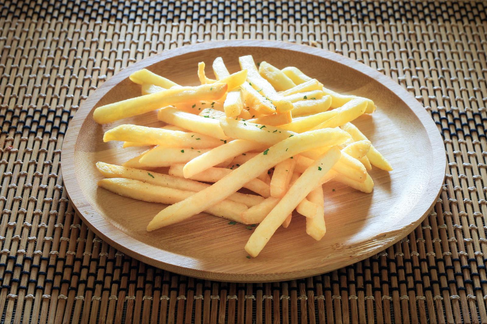 Fried potatoes with parsley served on a wooden plate placed on a bamboo placemat