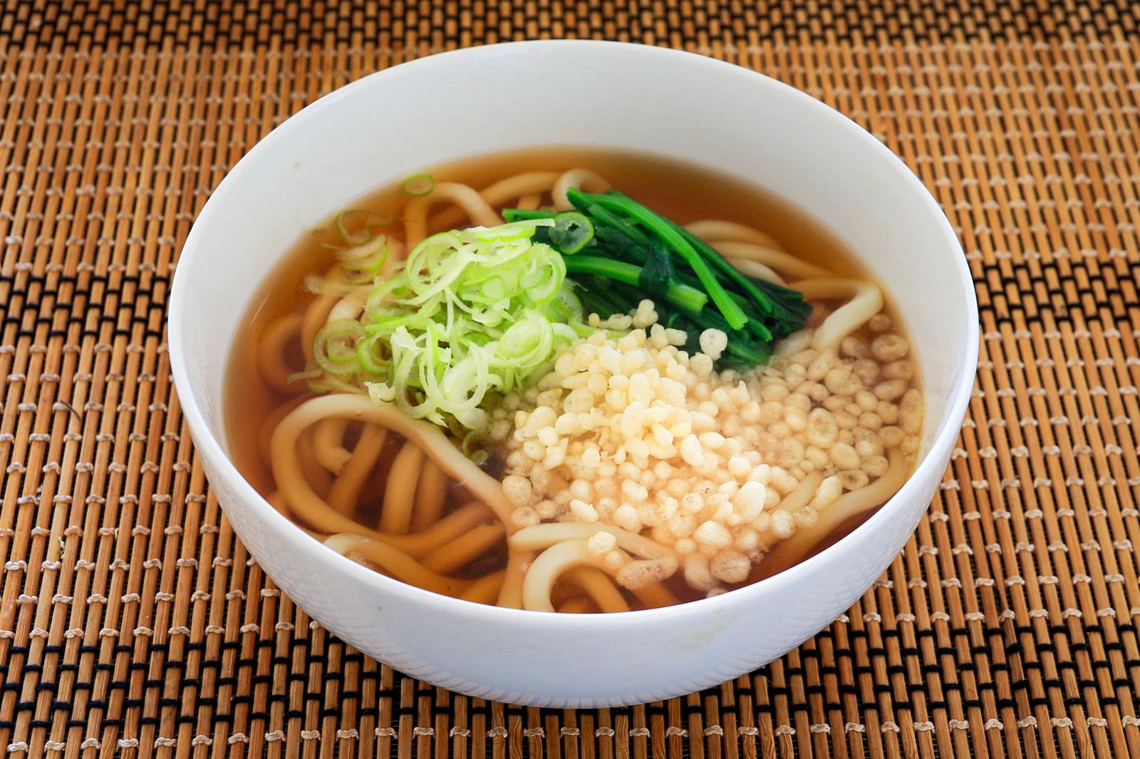 竹すだれの上に置かれた白い丼に盛られたねぎと天かすのかけうどん