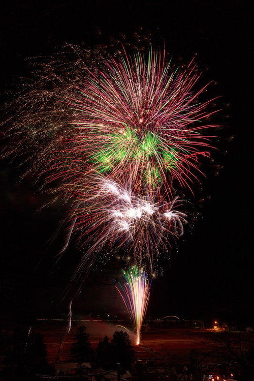 田んぼの中で打ち上がる赤と緑の花火が夜空を照らす光景