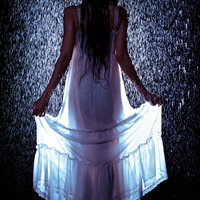 激しい雨に濡れてワンピースの裾をあげる女性の後ろ姿の写真