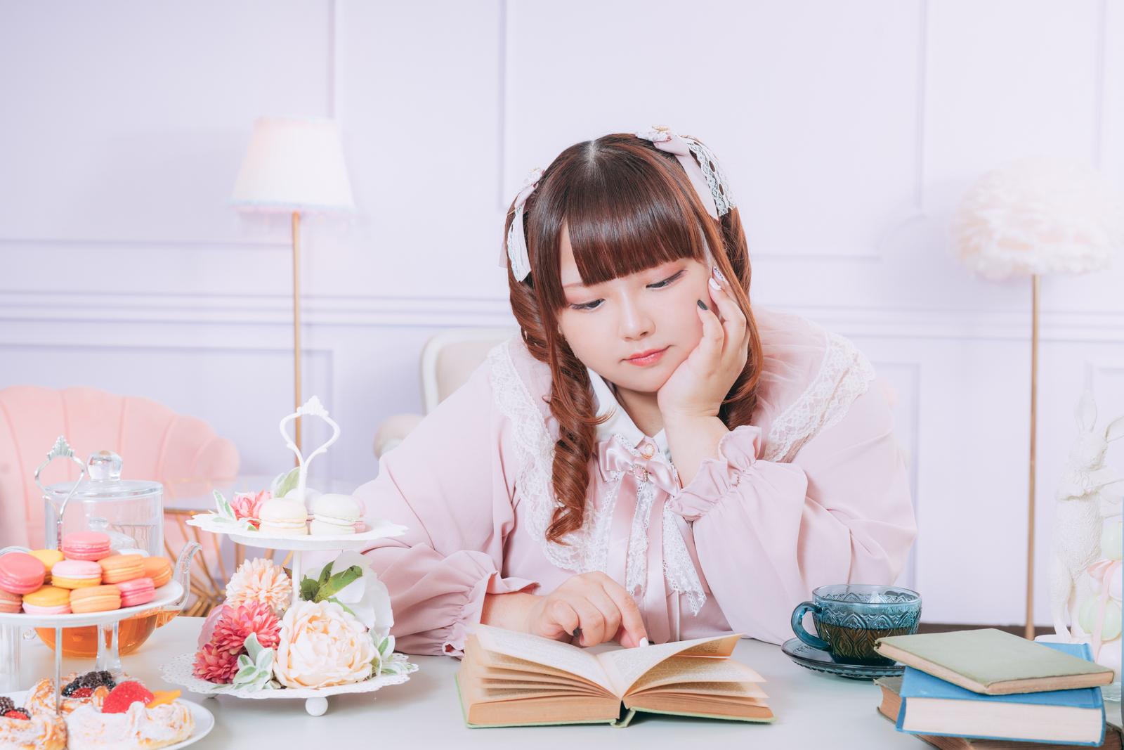 頬杖をつきながら本を読むピンクのロリータファッションの女性［モデル：あづき］