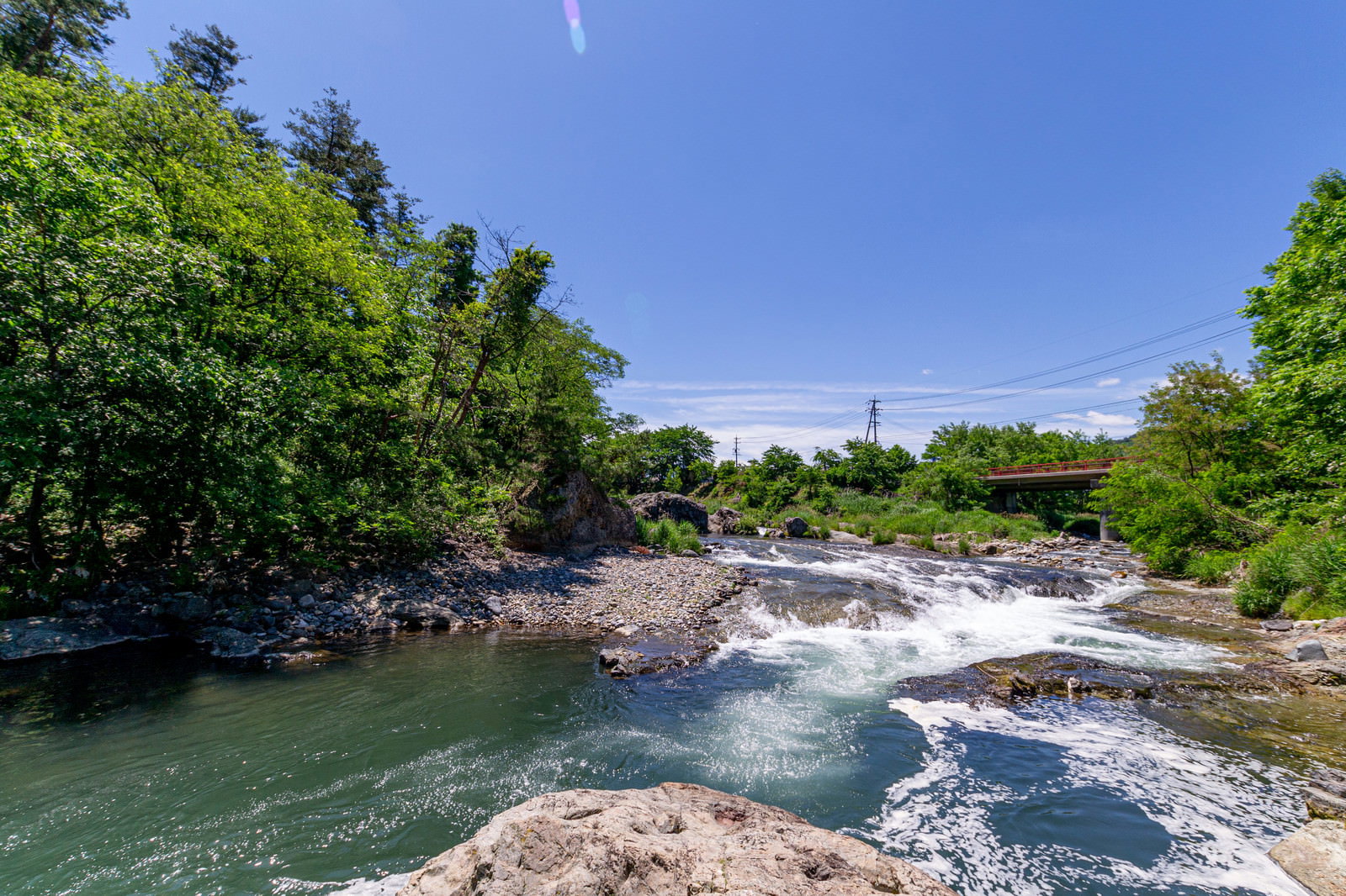 青空の下、緑の木々に囲まれた依田川の仙ヶ淵で岩場を流れる清流