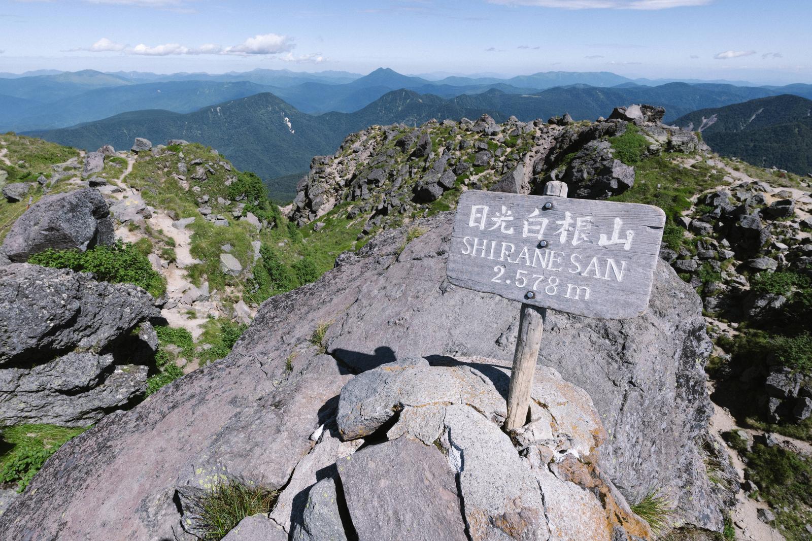 日光白根山の山頂に立つ標高2,578mの標識と、奥に見える連なった山々