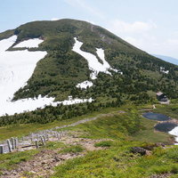 残雪の八甲田大岳と山小屋、初夏の登山道を歩く風景の写真