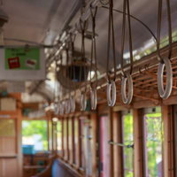 昭和レトロ電車の車内に下がる褐色の革製吊革と木製手すりの写真