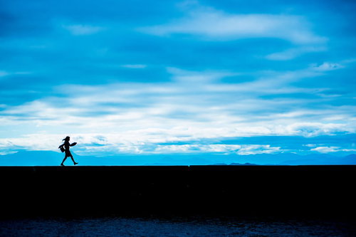 青空の埠頭で嬉しくてスキップするOLのシルエット