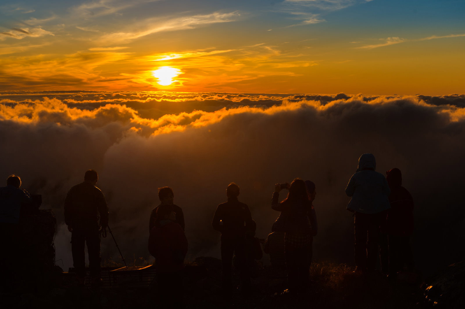 雲海に沈む夕日を眺める登山者たちのシルエット