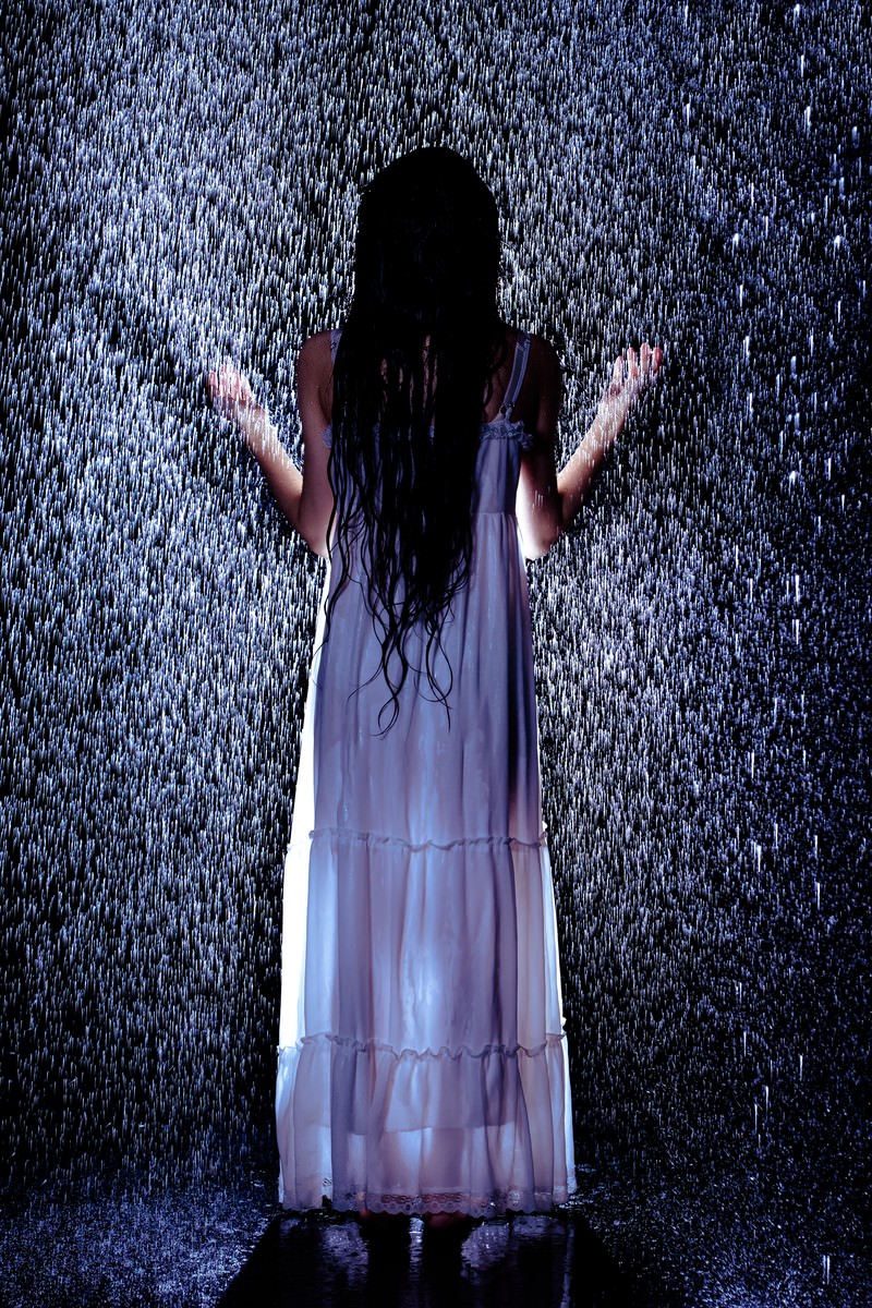 激しい雨の中で両手を広げて立つ白いワンピース姿の女性の後ろ姿［モデル：緋真煉］