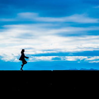 青空を背景に軽やかにスキップする女性のシルエットの写真
