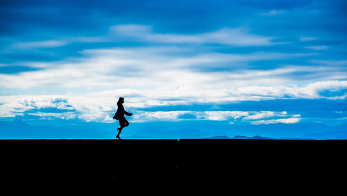 青空を背景に軽やかにスキップする女性のシルエット