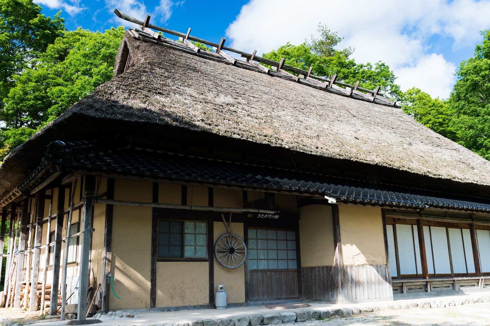 青空と緑に囲まれた茅葺屋根の古民家