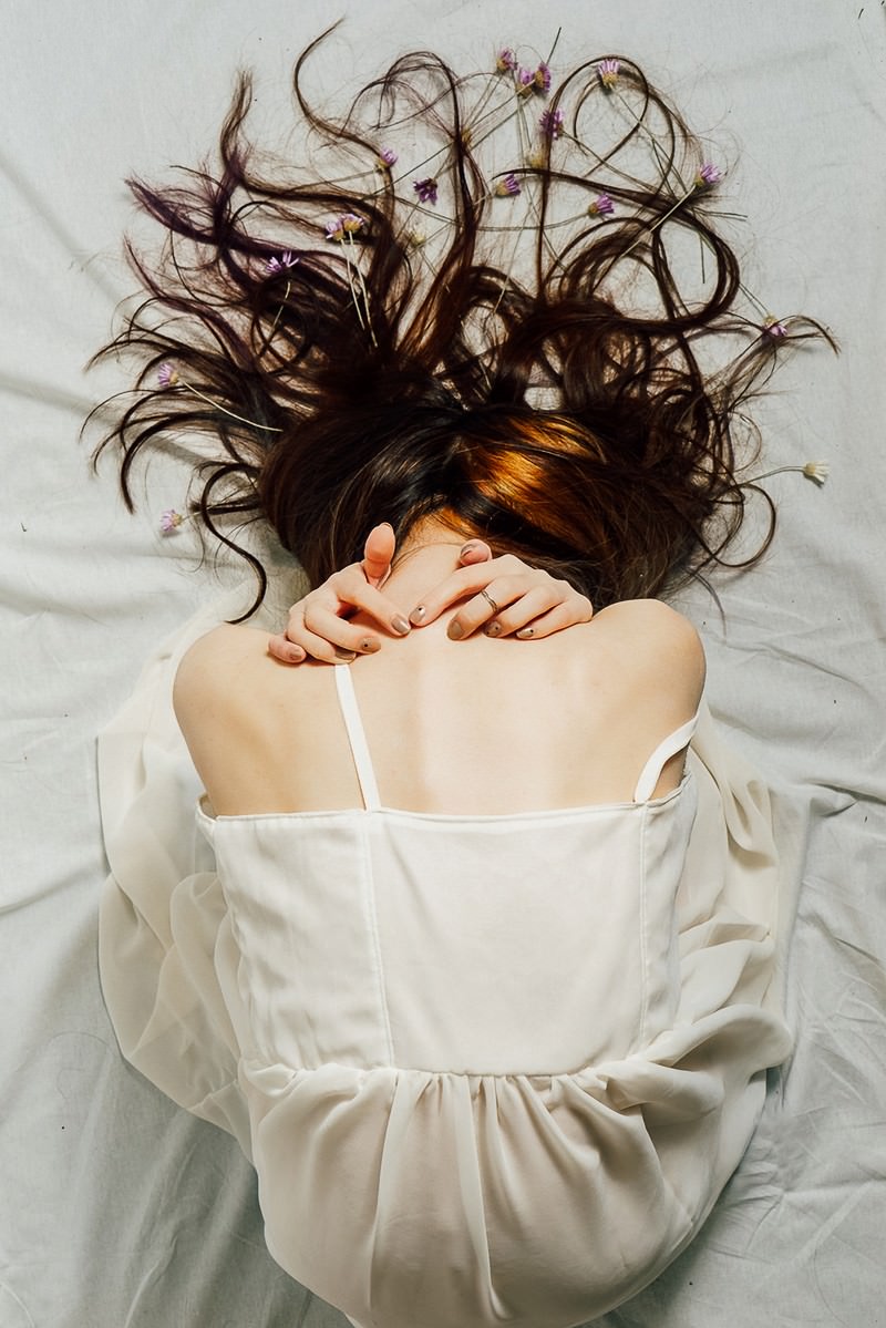 白い衣服を着た女性が床に蹲り、長い髪が垂れ下がる後ろ姿