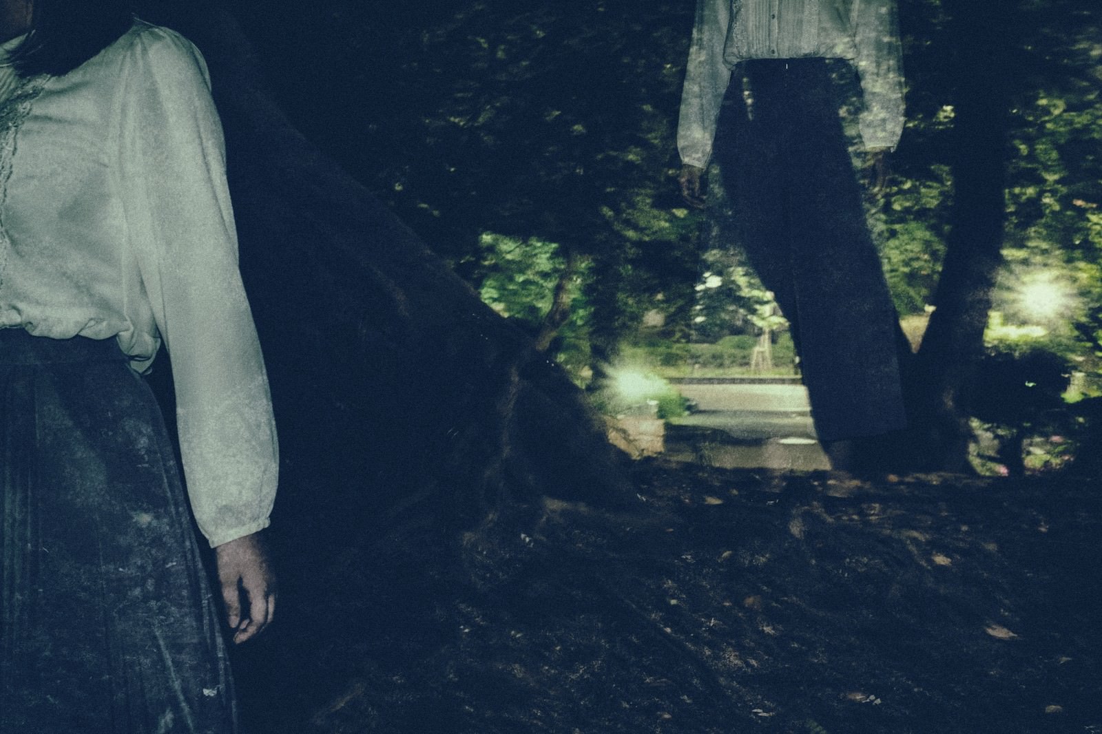 薄暗い森の中を白い衣服で歩く女性の後ろ姿［モデル：さとうゆい］