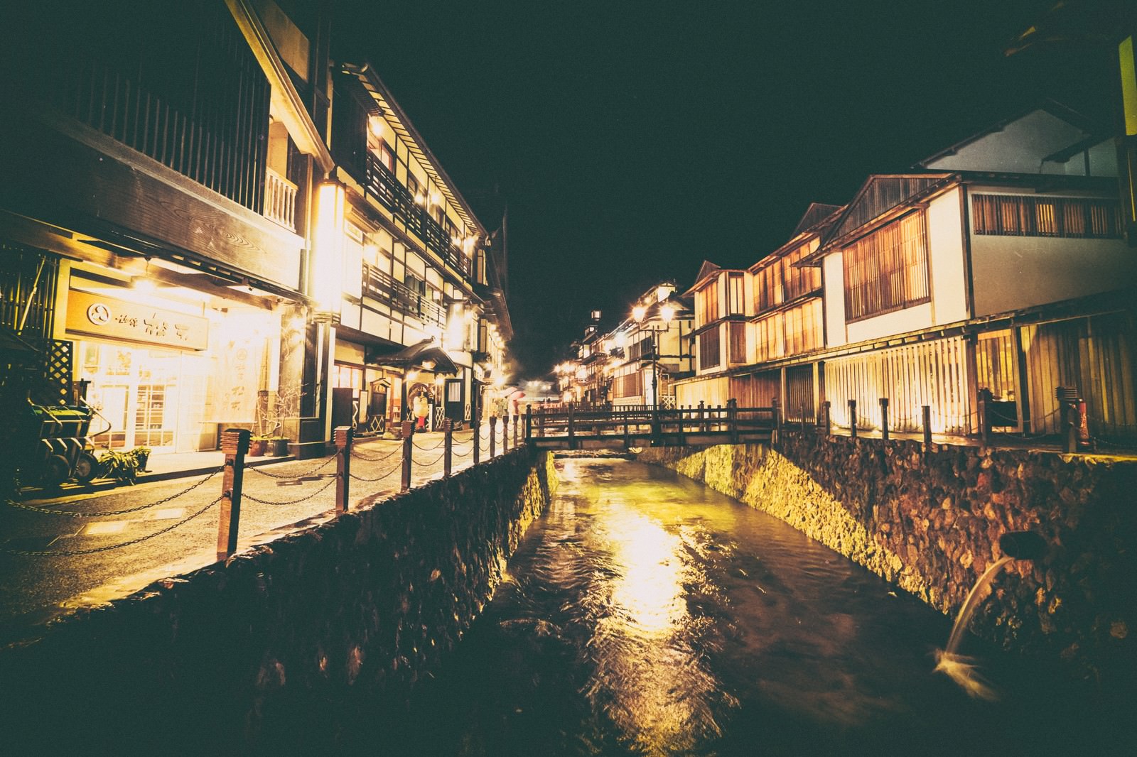 夜間にライトアップされた銀山温泉街の川沿いの旅館群