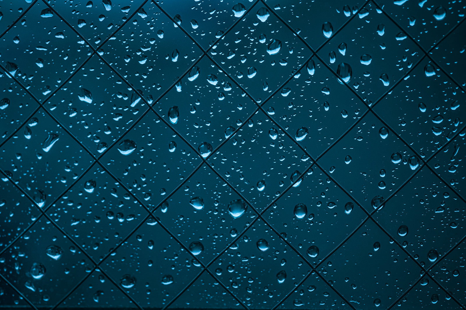 青いガラス面に無数の水滴が付着した雨の日の窓
