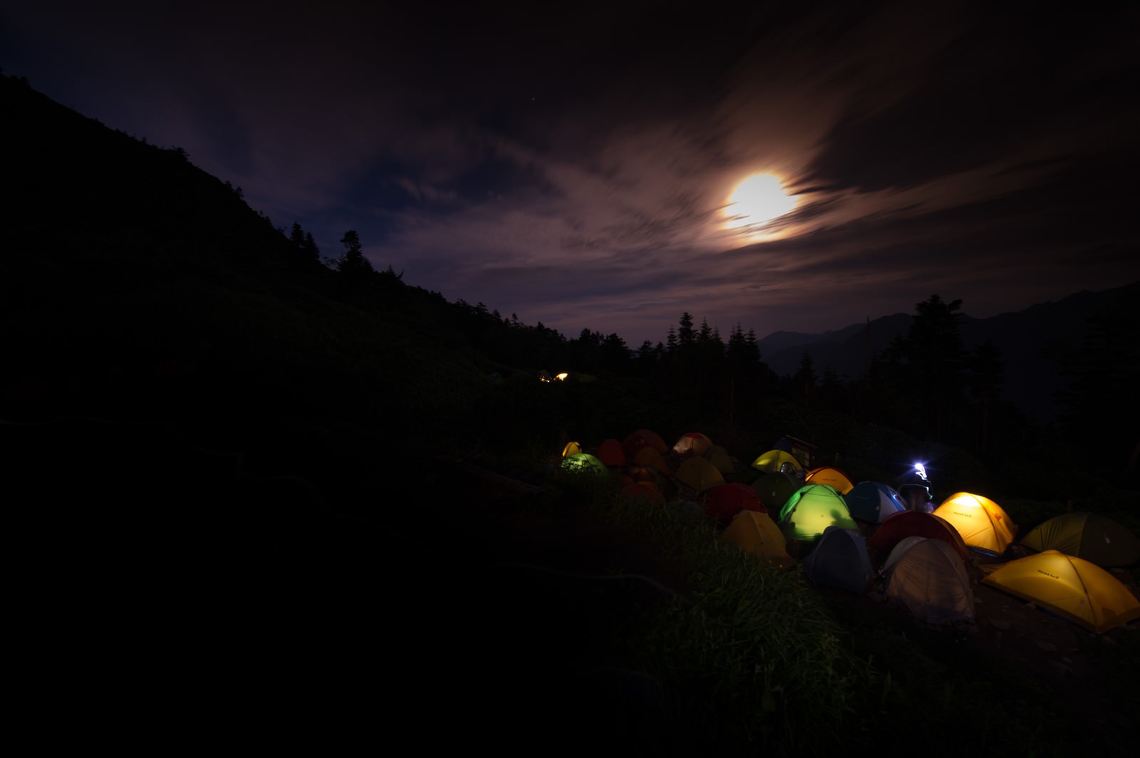 月明かりに照らされた山のテント場で複数のテントが設営されている夜景