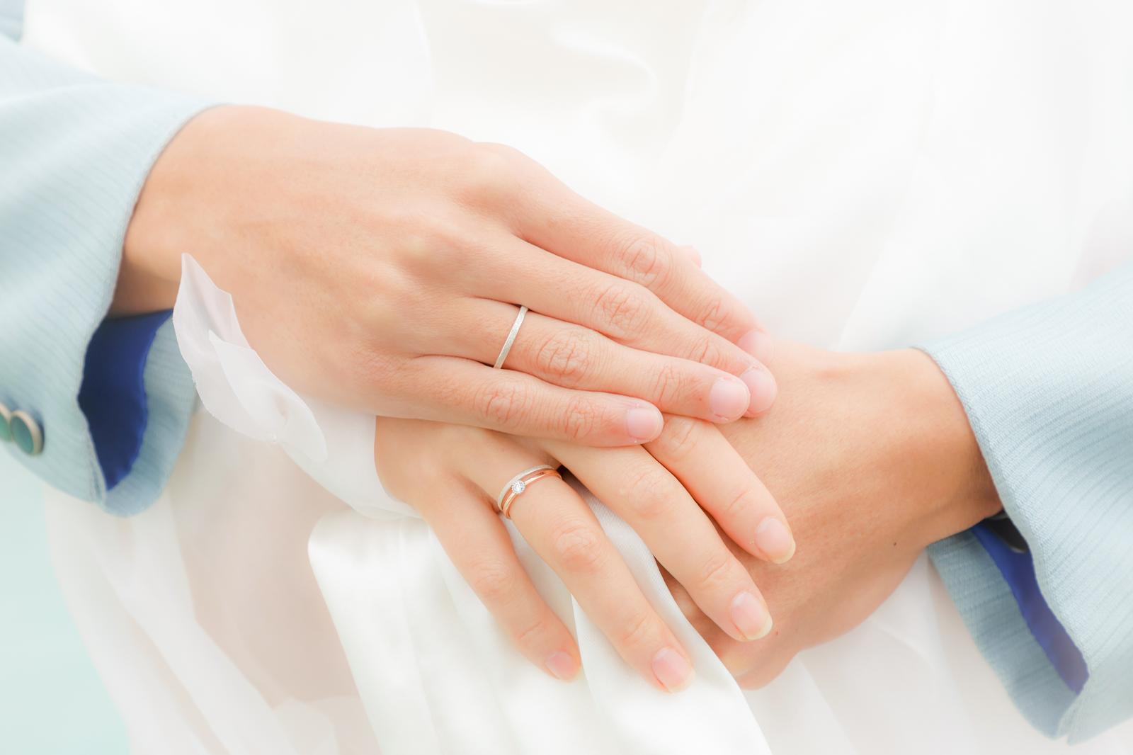 婚約指輪と結婚指輪をはめた新郎新婦が白いドレスの上で手を重ねている