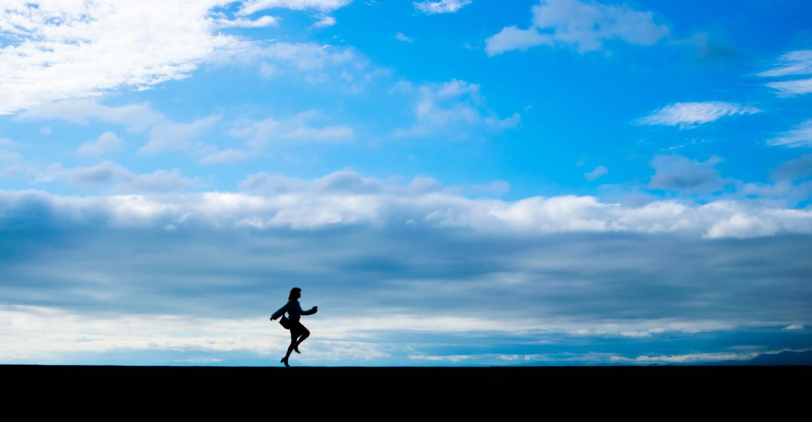 青空を背景にバッグを持ってスキップしている女性のシルエット