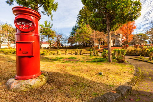 秋の公園に立つ赤い郵便ポスト