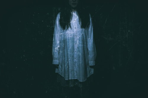 暗闇の中、青白い光に照らされて立ちすくむ白いドレスの女性