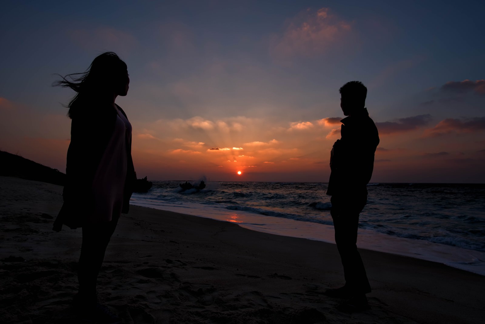 夕暮れの海辺で夕日をバックに立つ男女のシルエット