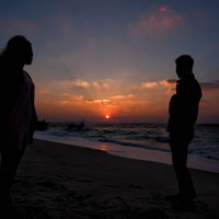 夕暮れの海辺で夕日をバックに立つ男女のシルエットの写真