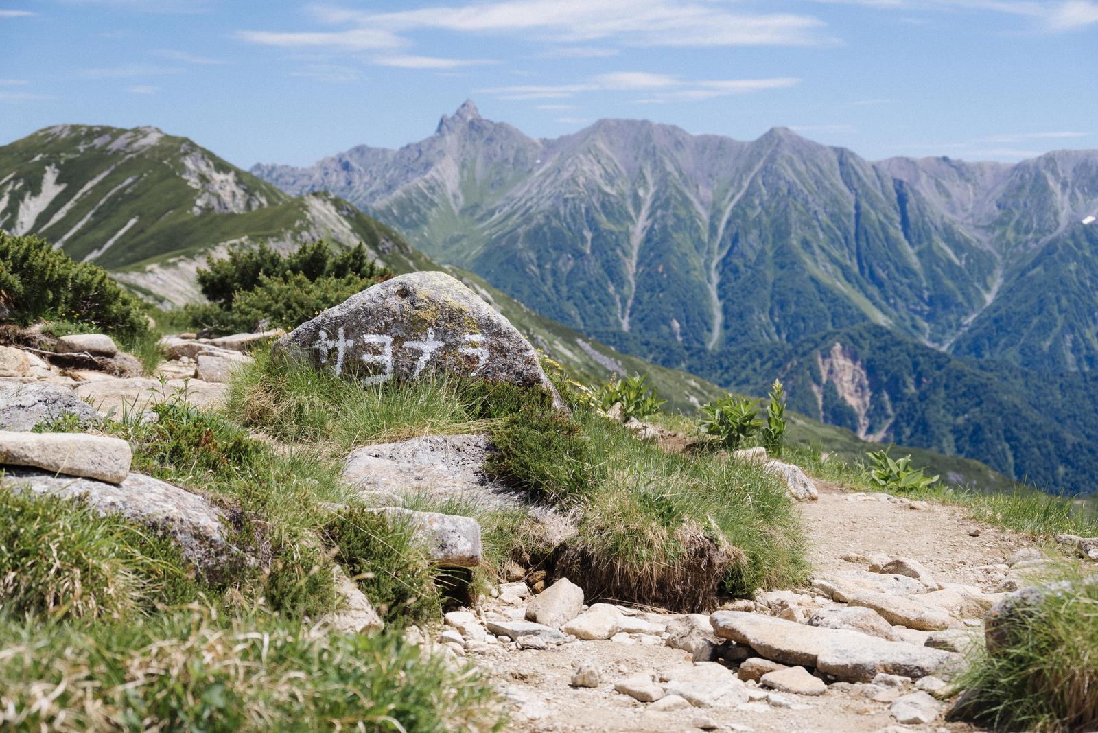 笠ヶ岳の登山道に置かれた挨拶の岩と遠くの山々の風景