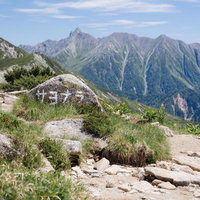 笠ヶ岳下山者へ挨拶する岩と遠くの山々、樹林帯の峰々の写真
