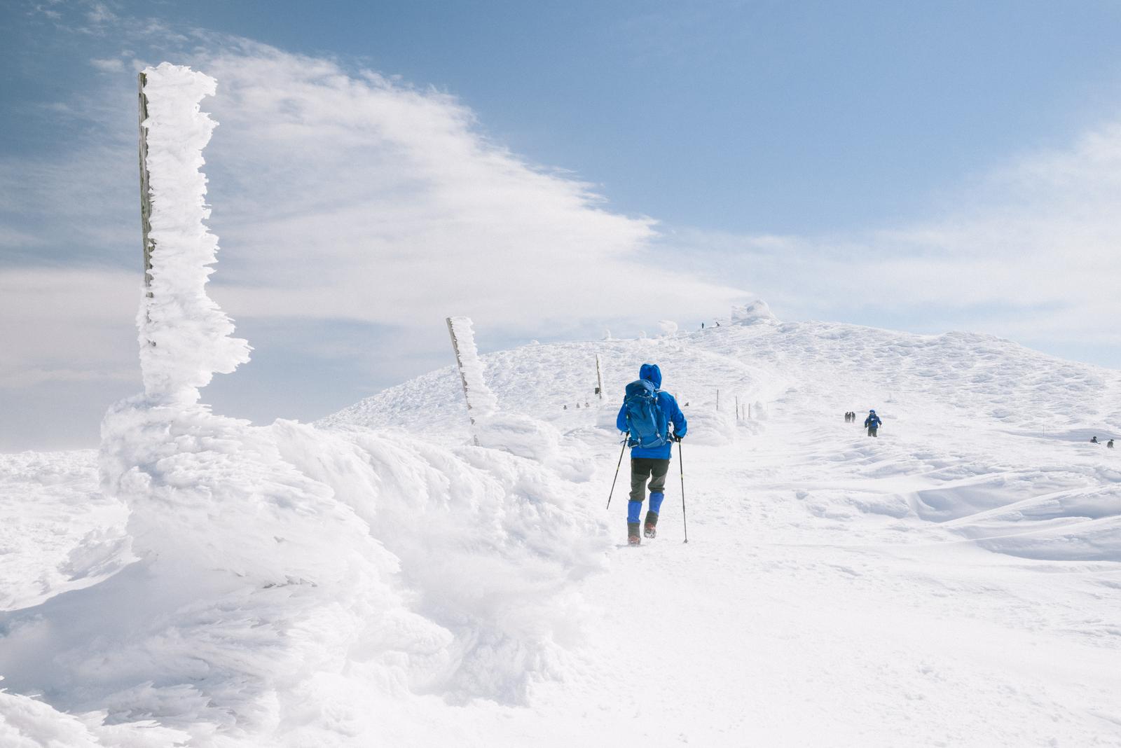 青いジャケットの登山者が雪に覆われた蔵王の馬の背を登っている