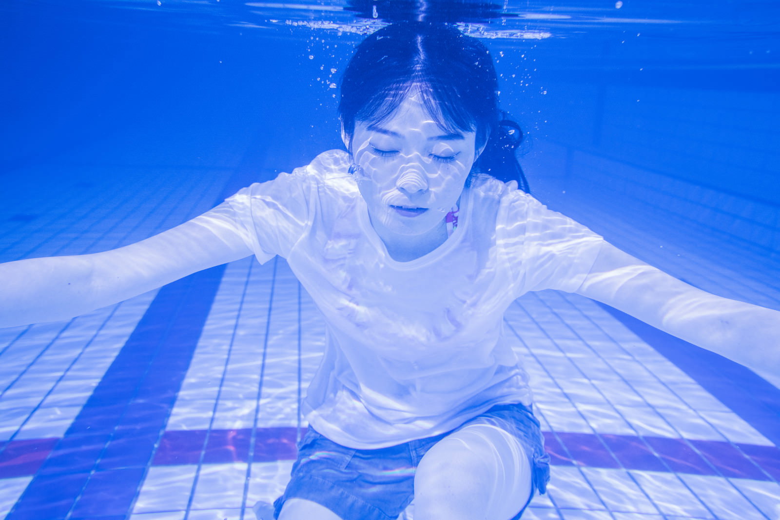 Woman in a white t-shirt holding her breath underwater in a pool