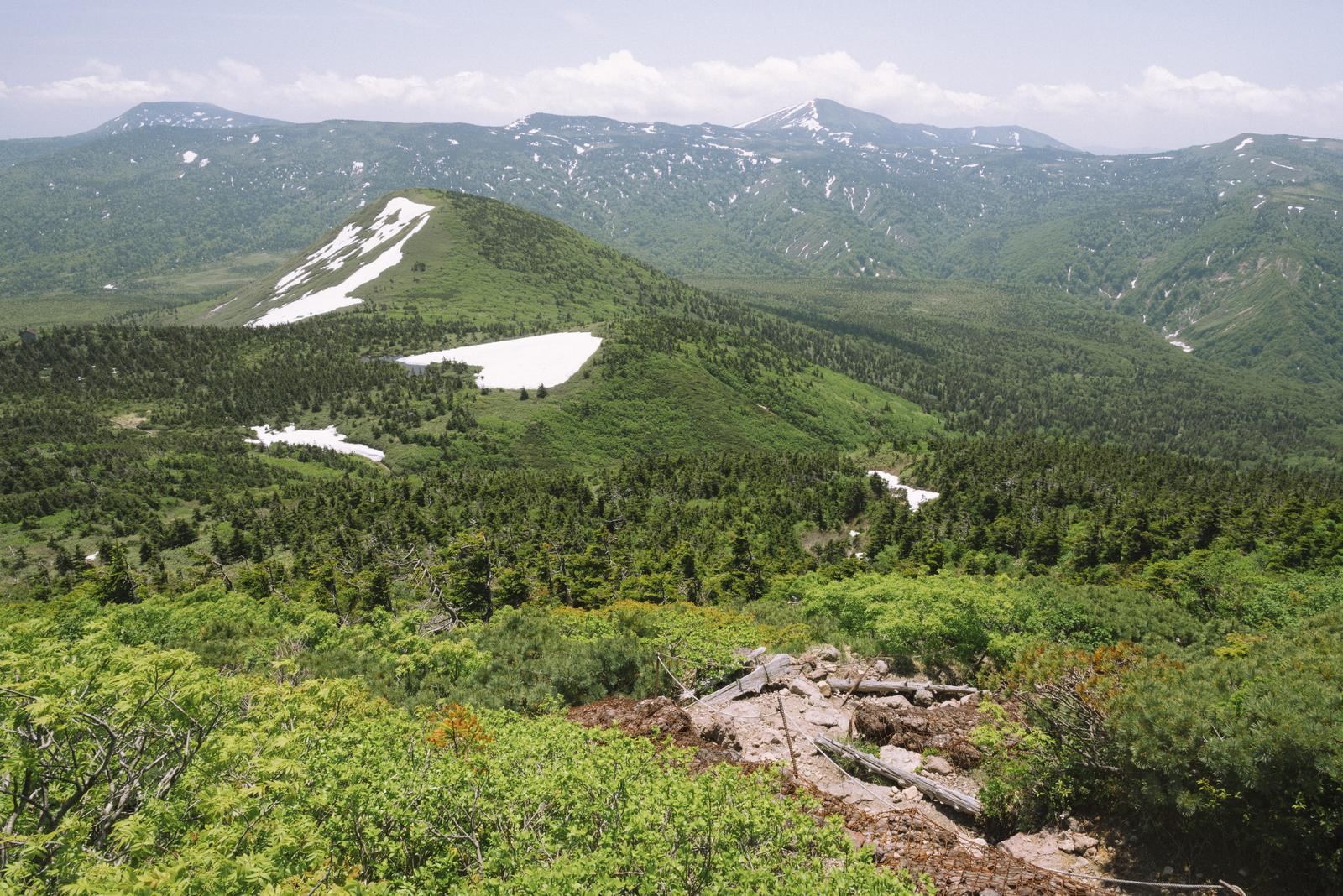 八甲田山大岳からの眺望。手前の山に残雪があり、緑の森林に囲まれた山々が続く