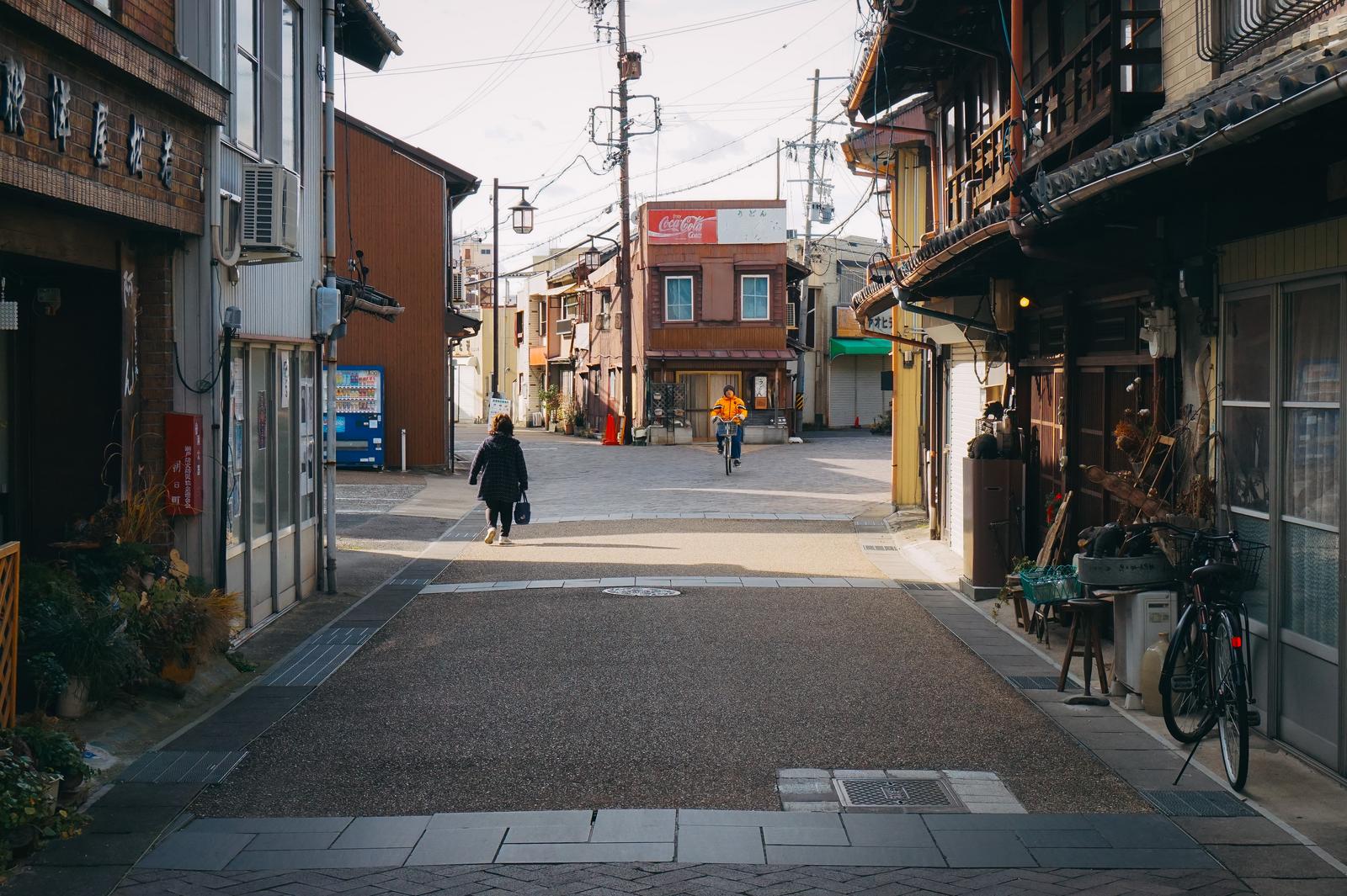 下町の古い住宅街の通りを歩く人々と駐輪された自転車