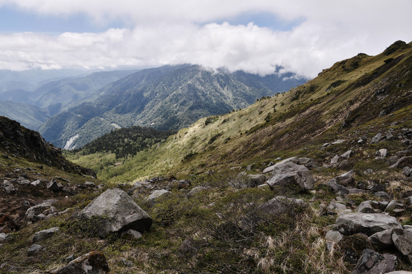 岩や石が散らばる茶褐色の焼岳の山肌と遠景の山並み
