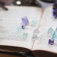 古書の上に置かれた紫と青のフローライト結晶の写真