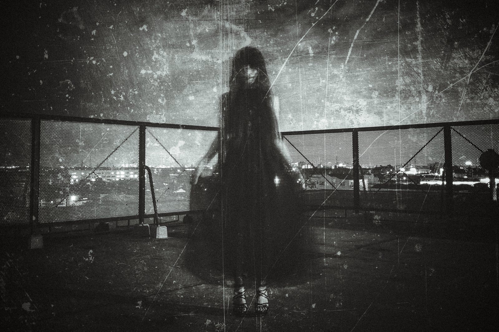 夜の屋上でフェンスの前に立つ黒いドレスを着た女性のシルエット［モデル：緋真煉］