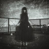 夜の屋上でフェンス前に立つ黒いドレスを着た女性の姿の写真